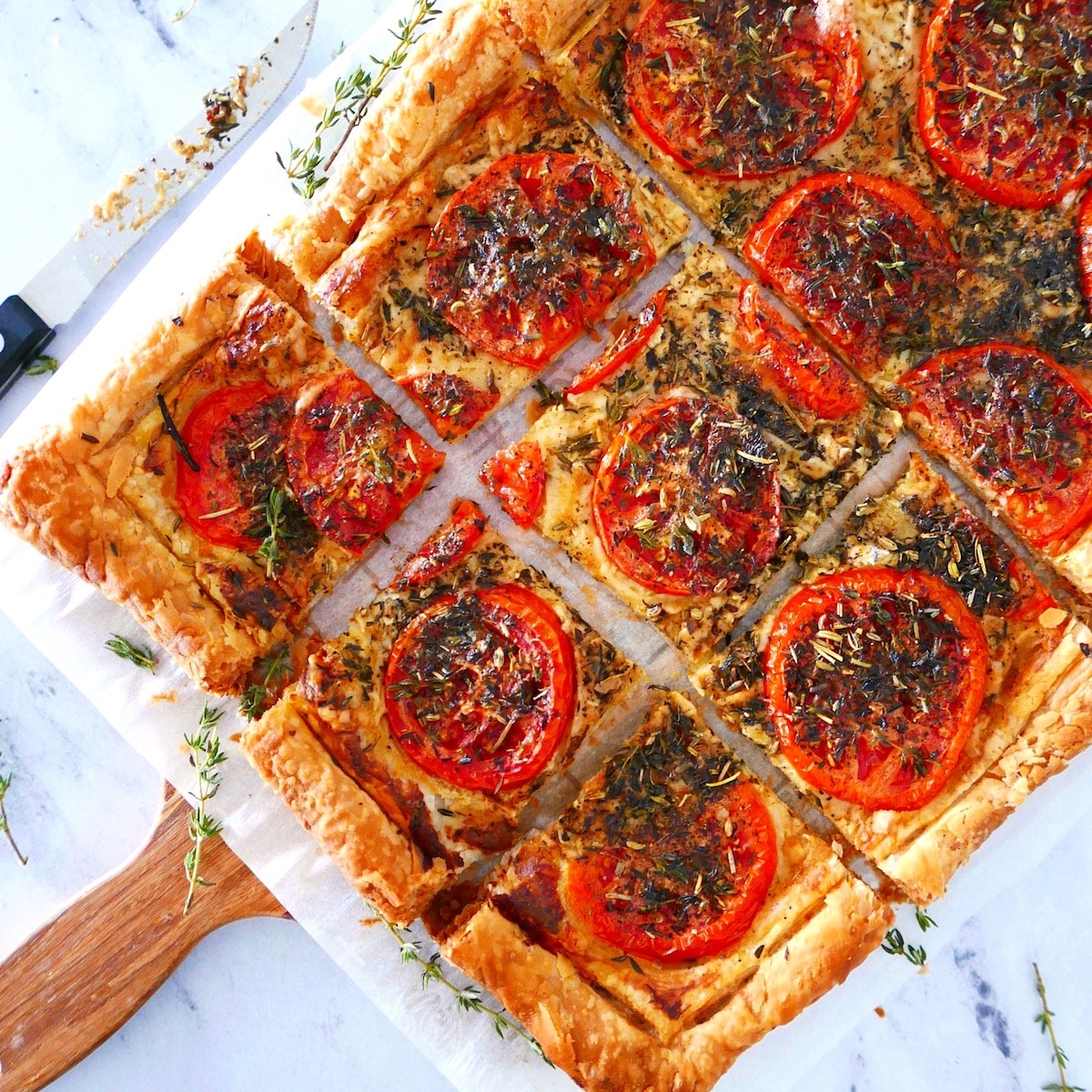 french tomato tart with puff pastry cut into squares with a knife resting nearby