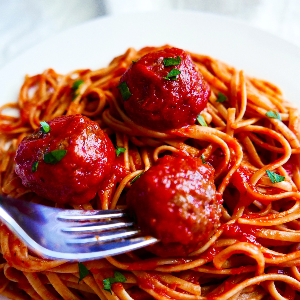 Fork digging into plate of meatballs with spaghetti.