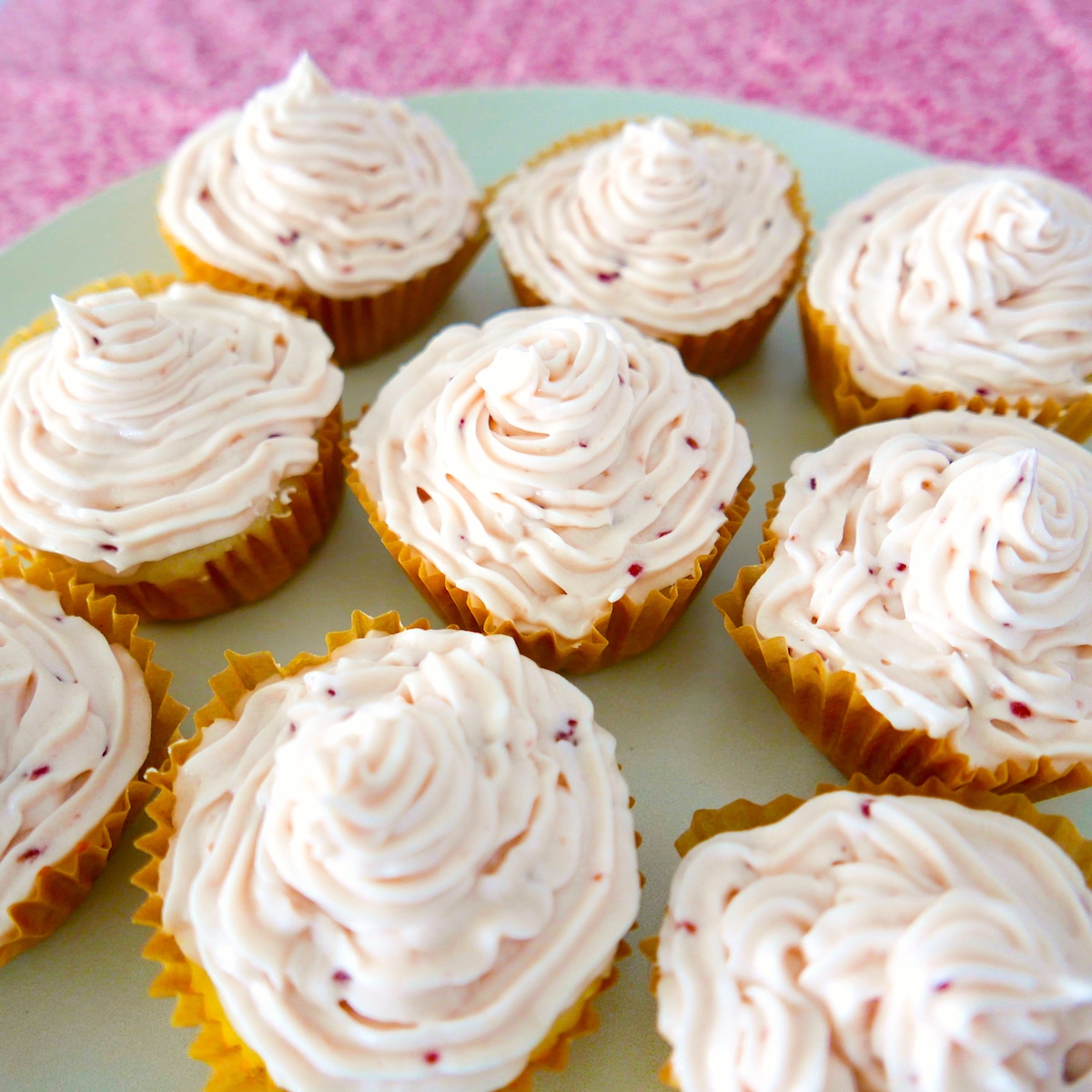 raspberry almond cupcakes arranged on a white platter with pink background