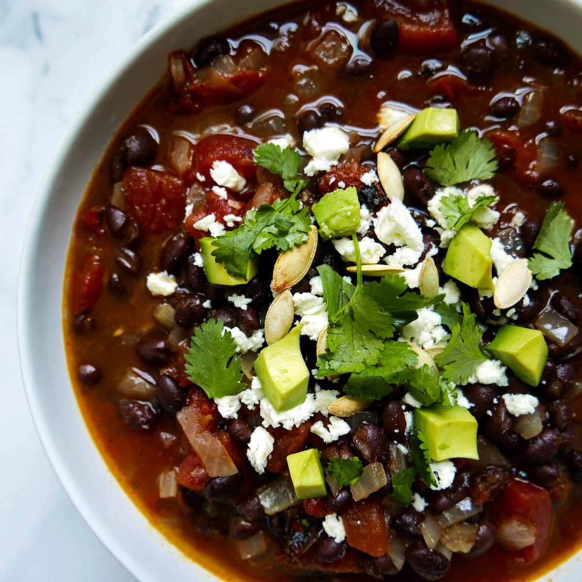 Bowl of black bean soup garnished with cheese, avocado, and cilantro.