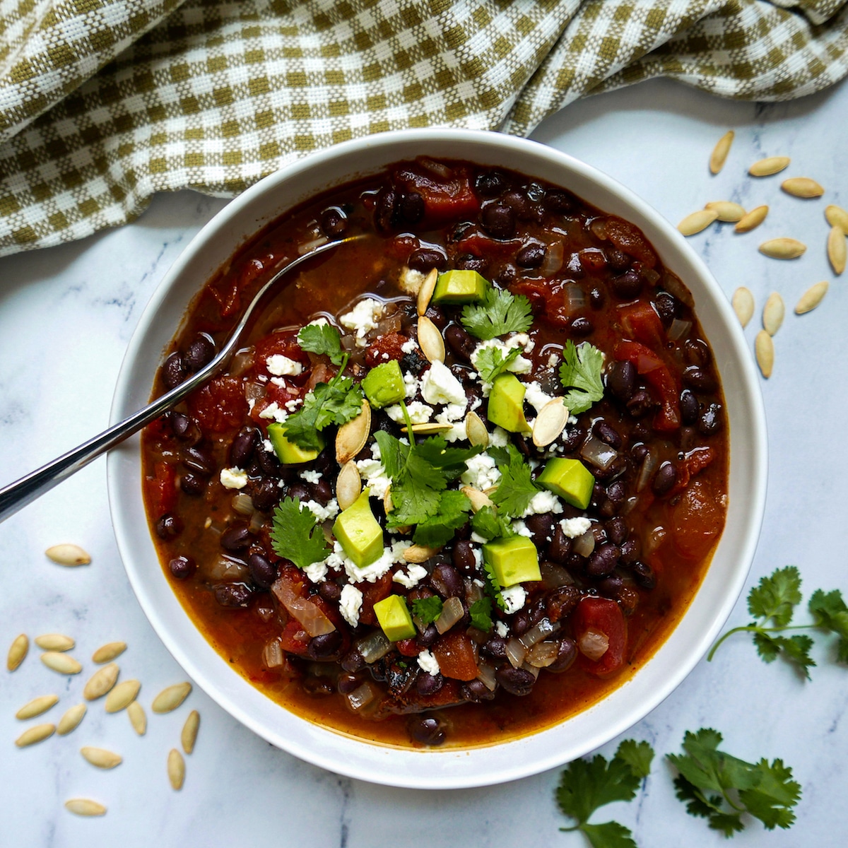 black bean soup in a white bowl garnished with pumpkin seeds and cilantro and a spoon.