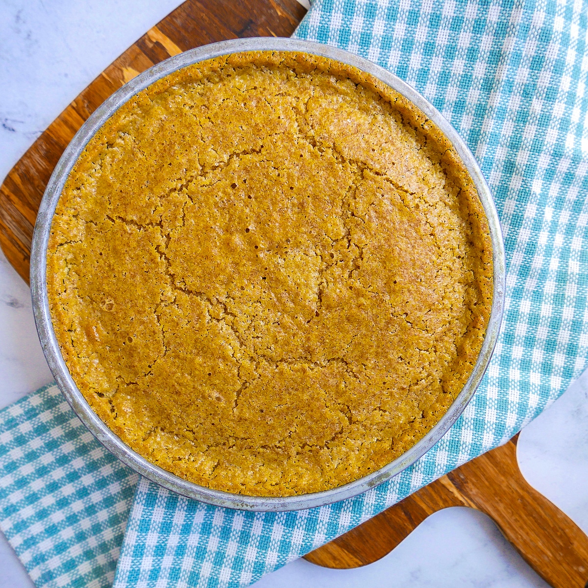 Cornbread in a round pan with gingham dish towel underneath.