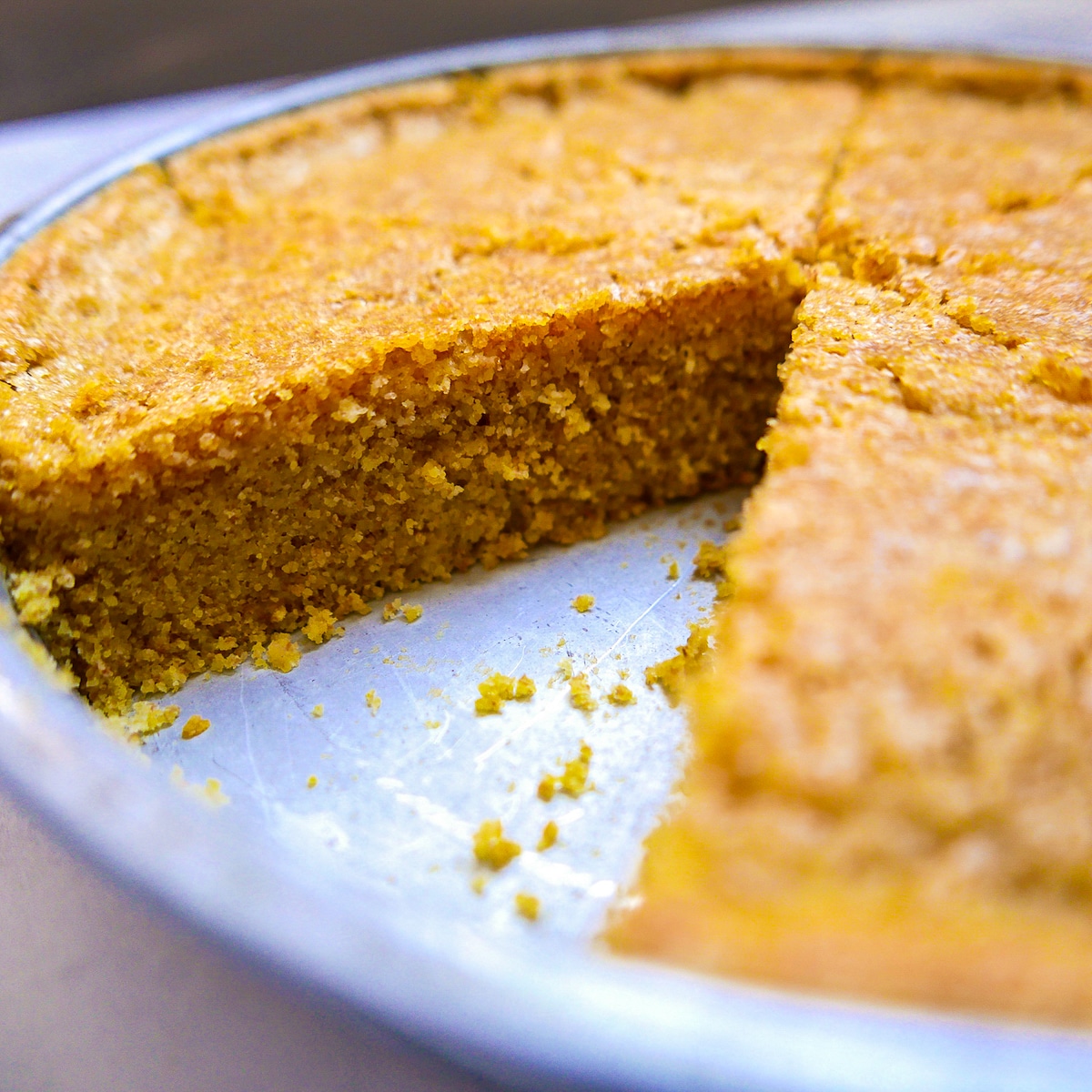 sourdough cornbread in cake pan with one slice missing.