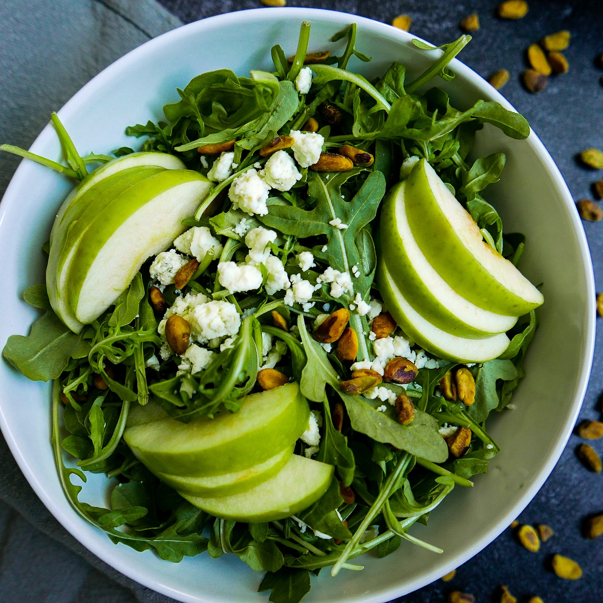 Apple salad with gorgonzola, pistachios and mustard vinaigrette in a white bowl. 