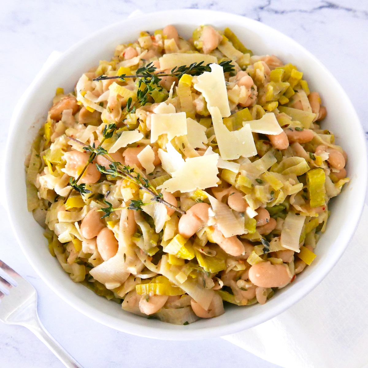 braised-white-beans-and-leeks.jpg braised white beans and leeks garnished with parmesan and thyme in a white bowl with fork