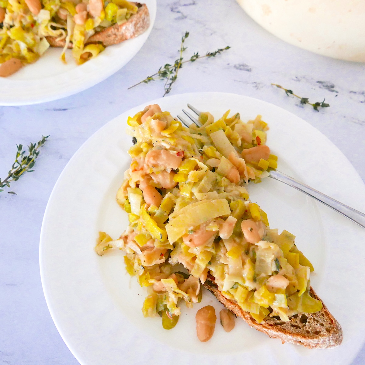 braised-white-beans-and-leeks.jpg braised white beans and leeks on sourdough toast on a white plate with fork