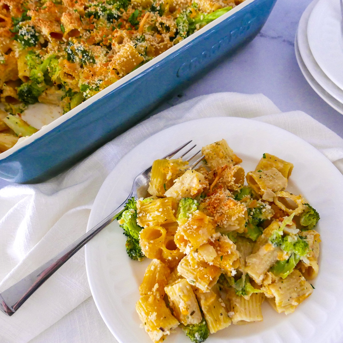 broccoli-pasta-bake-2.jpg broccoli pasta bake on white plate with fork with pan in background