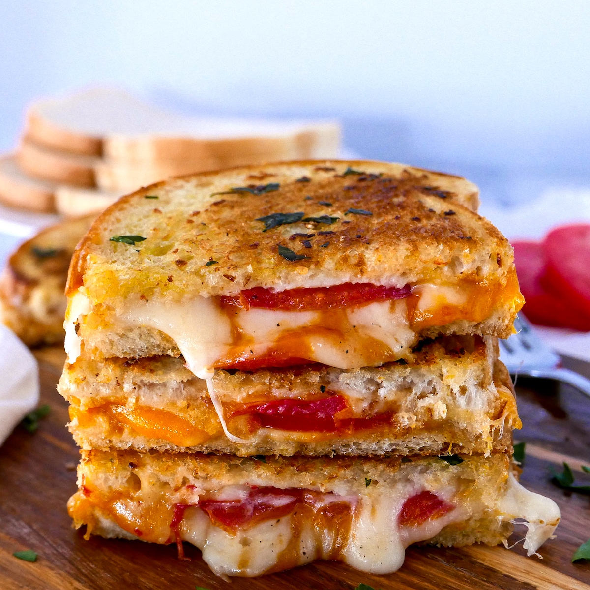 garlic-grilled-cheese-stack.jpg three pieces of garlic grilled cheese stacked on a cutting board with sourdough slices in background