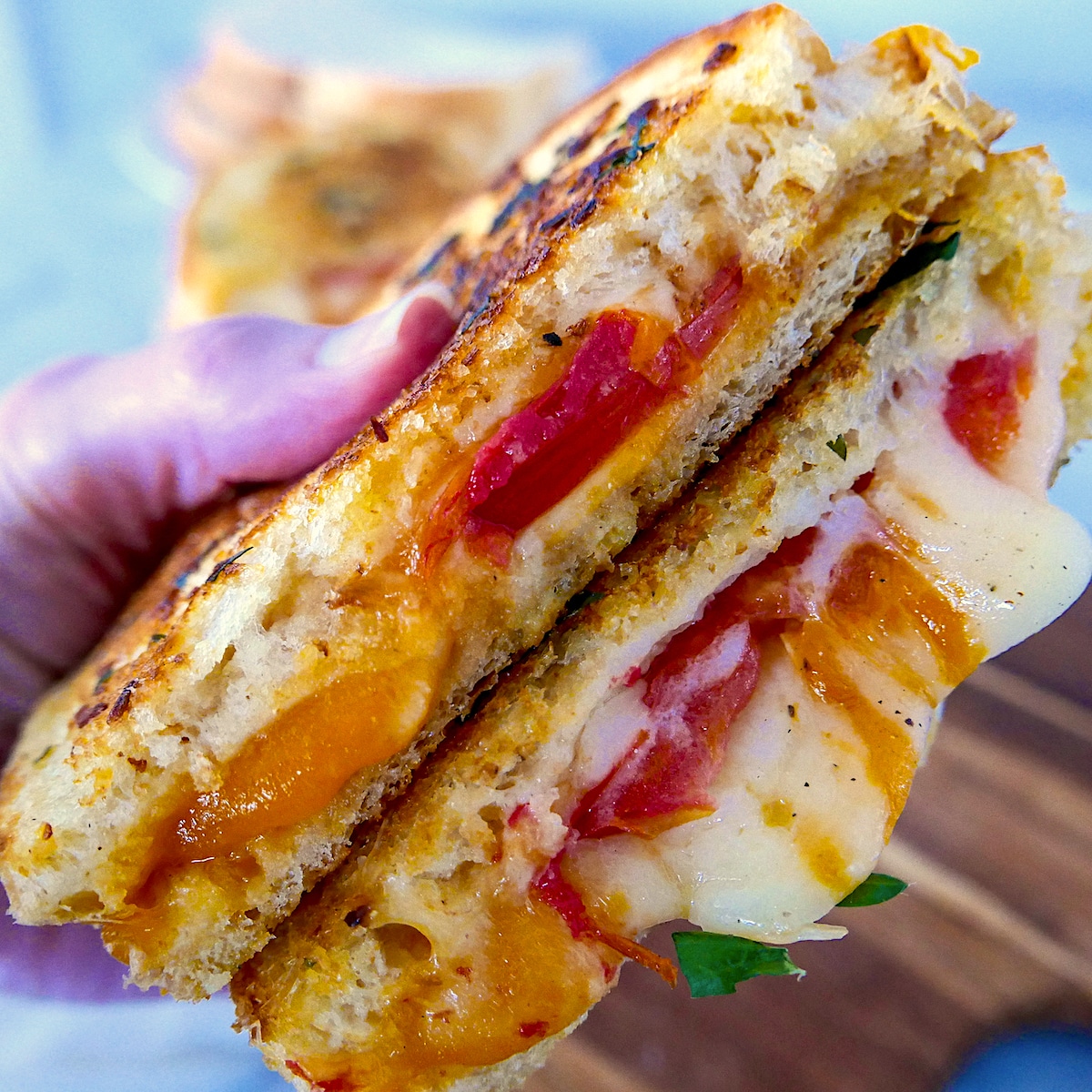 White hand holding a grilled cheese sandwich with another grilled cheese in the background.