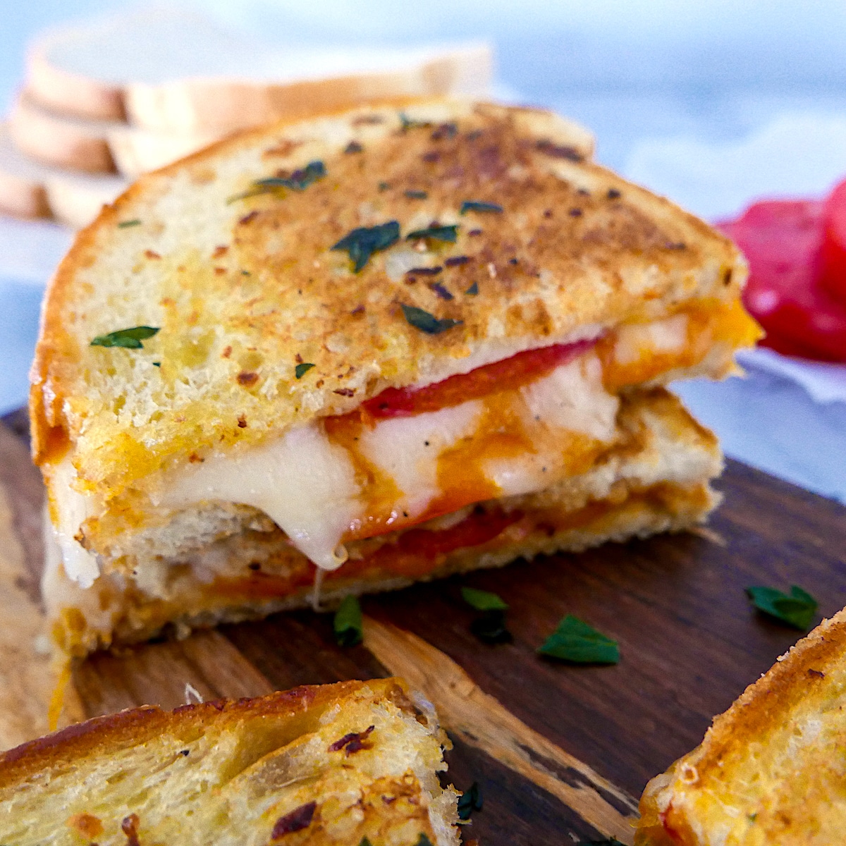 garlic-grilled-cheese-on-cutting-board.jpg garlic grilled cheese cut in half on a wooden cutting board with tomato slices in background