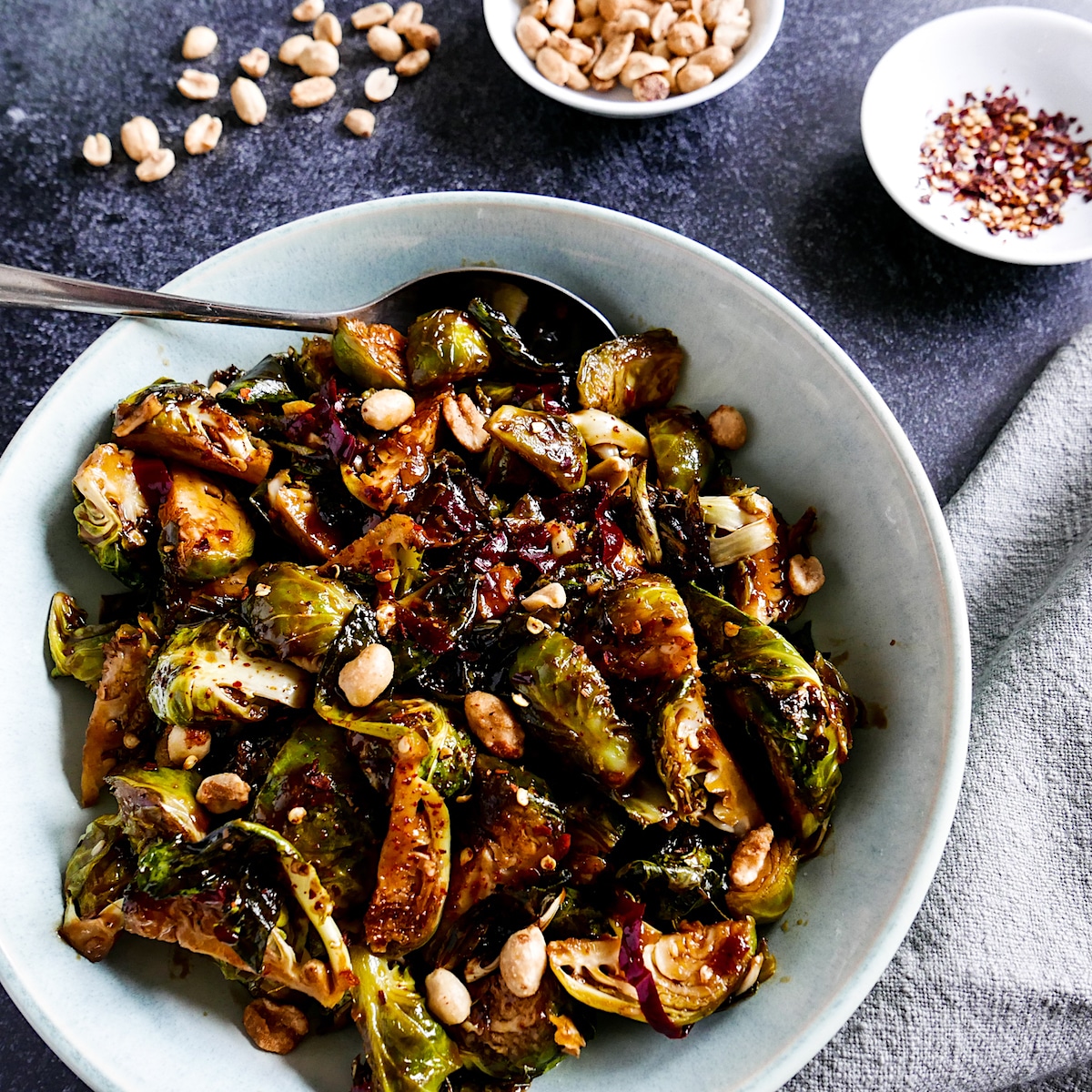 Brussesl sprouts with kung pao sauce in a white bowl with a spoon.