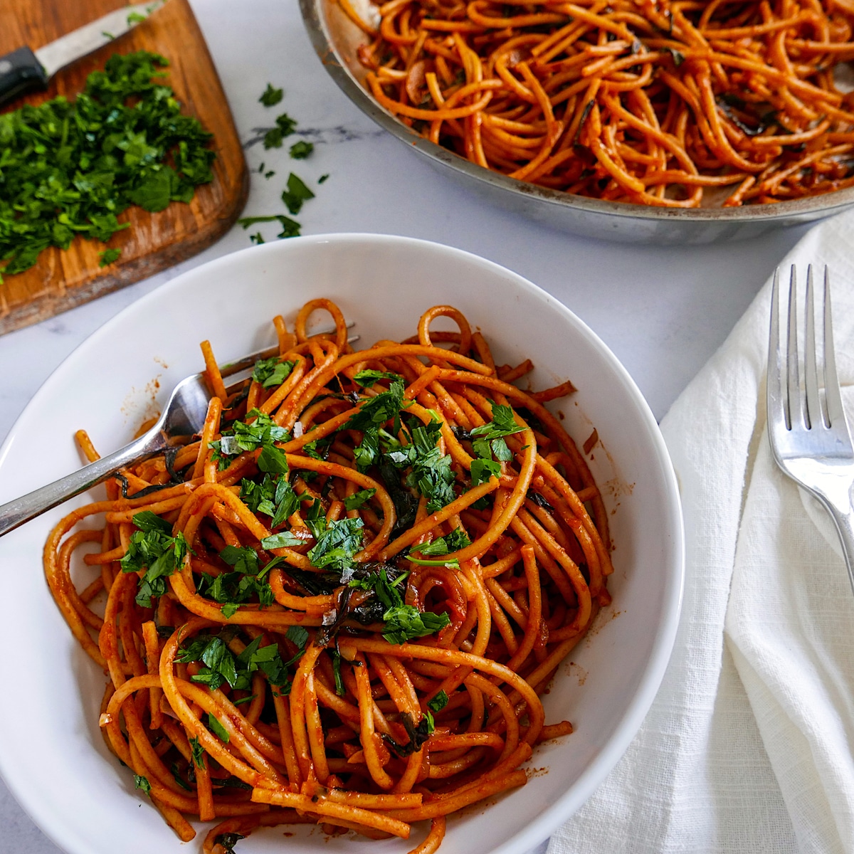 Bowl of shallot pasta with fork and more pasta in a pan in the background.