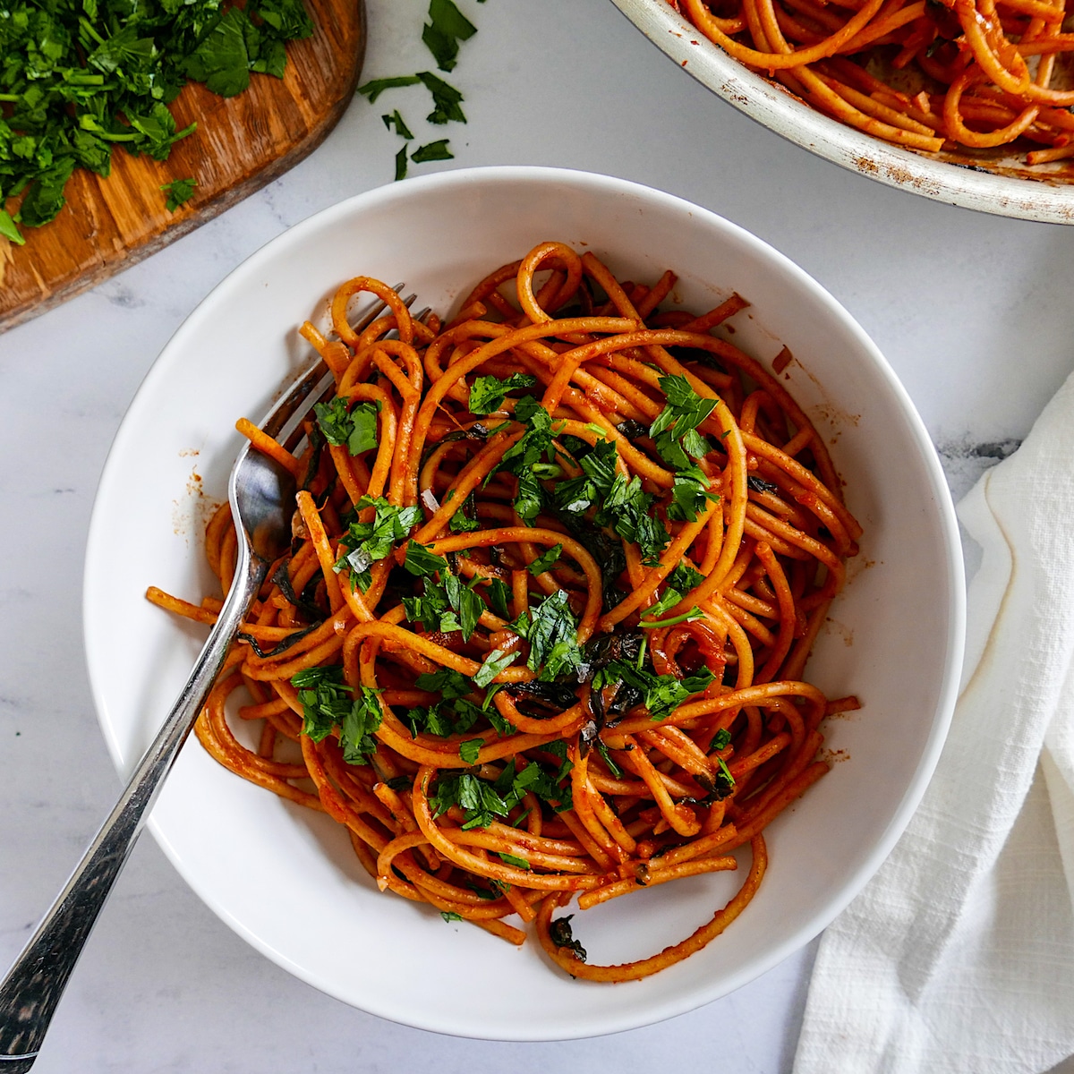 White bowl of pasta with shallots garnished with parsley and resting on a white napkin. 