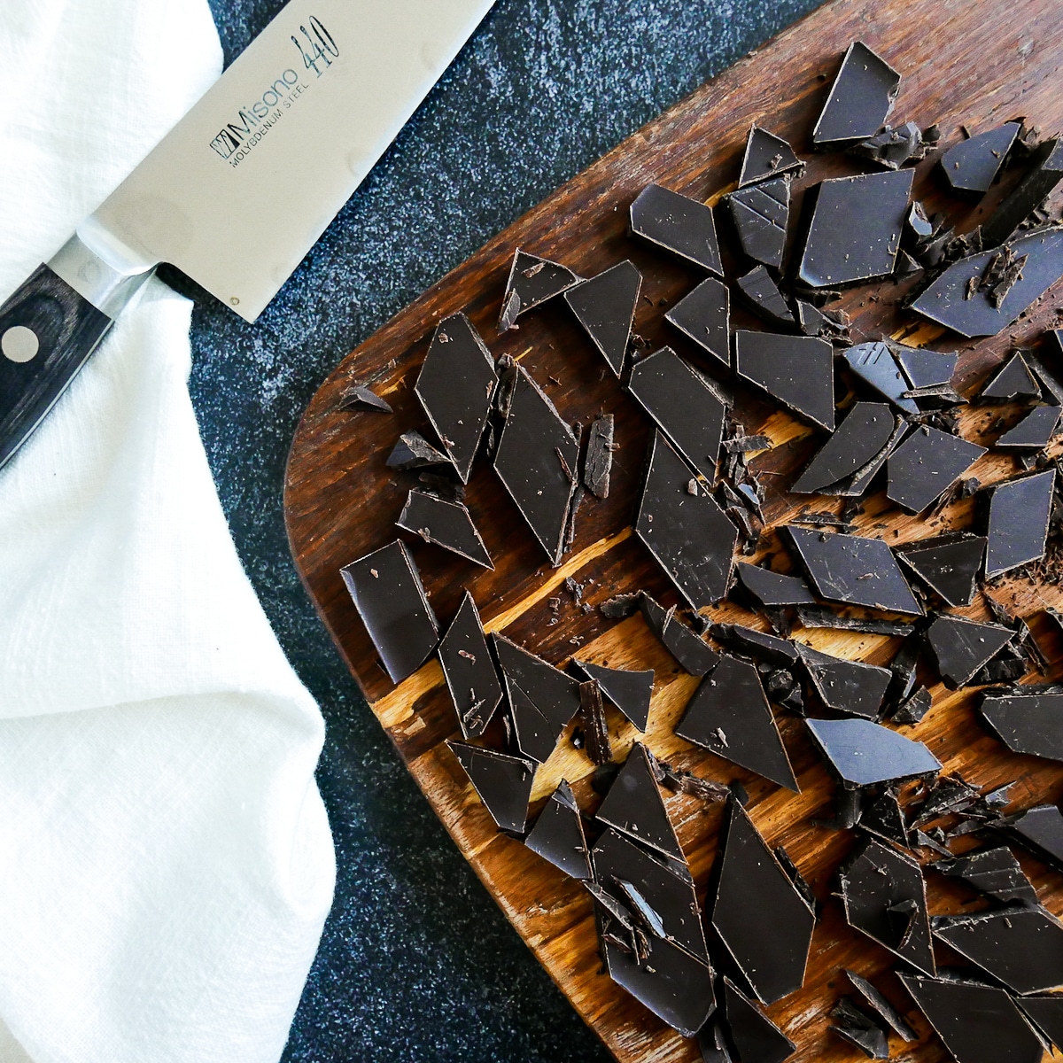 dark chocolate cut into pieces on a wooden cutting board with knife.