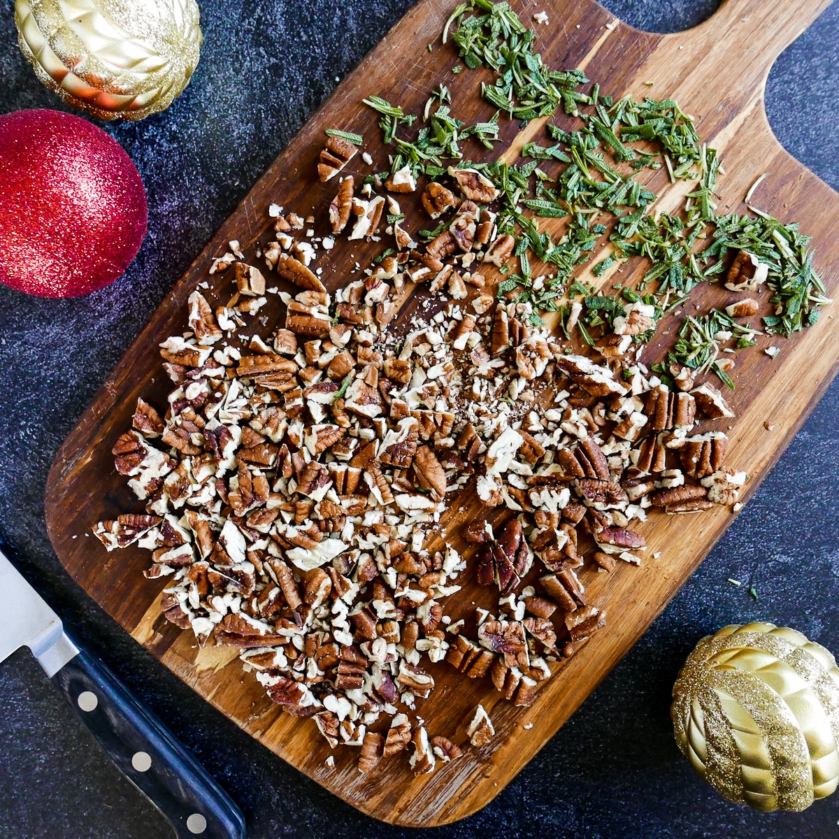 chopped pecans and rosemary on a wooden cutting board with knife.