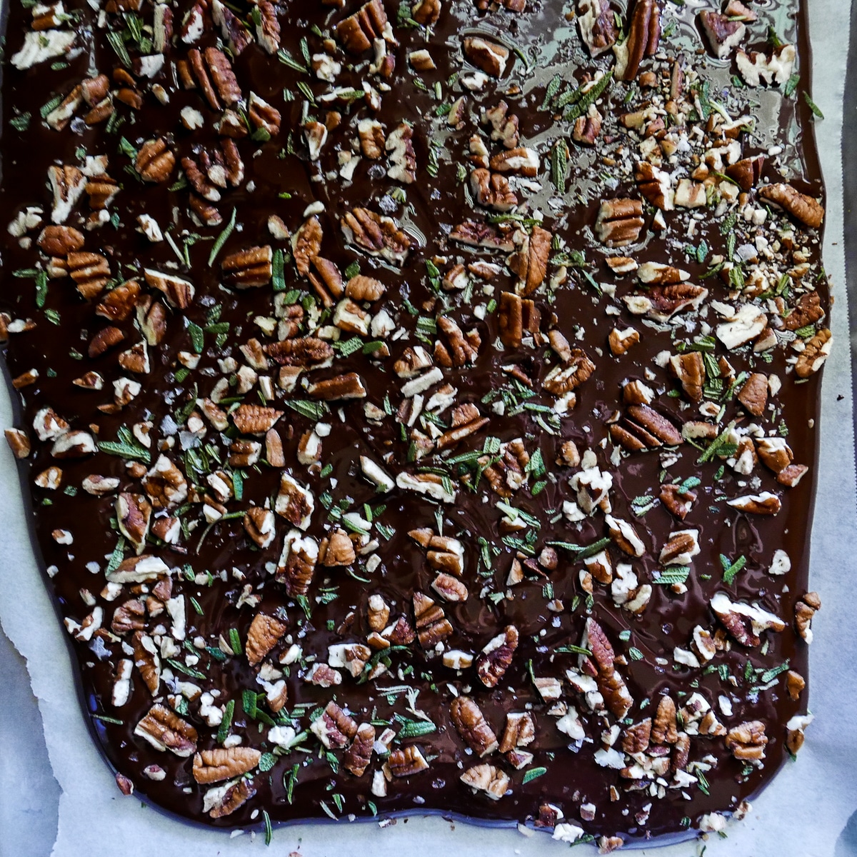 chocolate topped with pecans and rosemary on a baking sheet