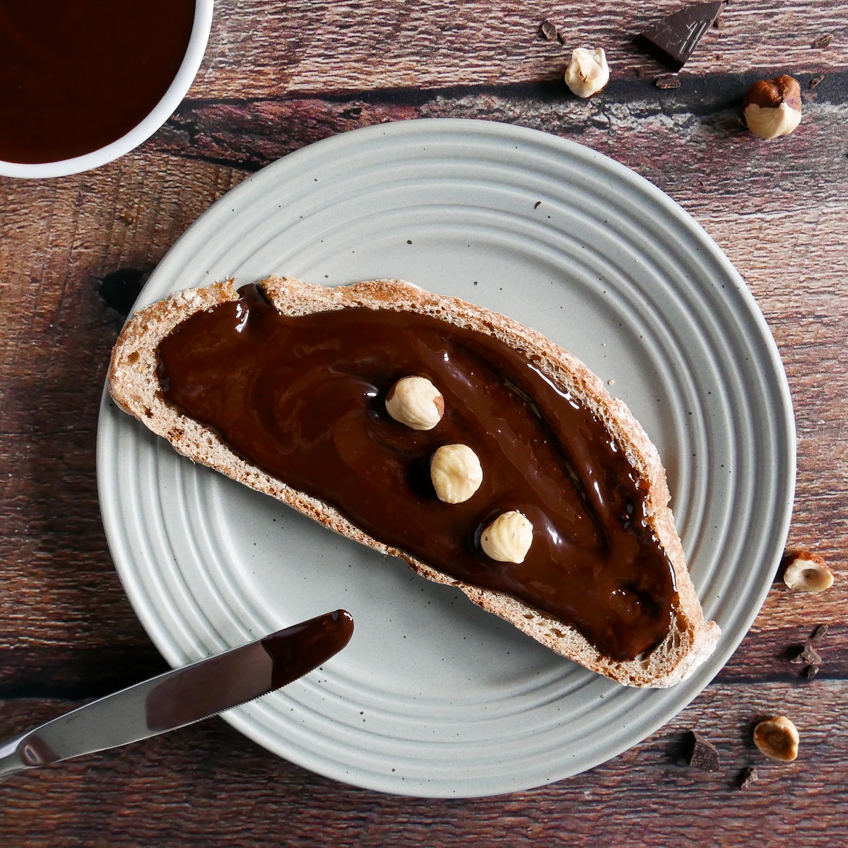 Hazelnut spread on a piece of bread on a gray plate with knife.