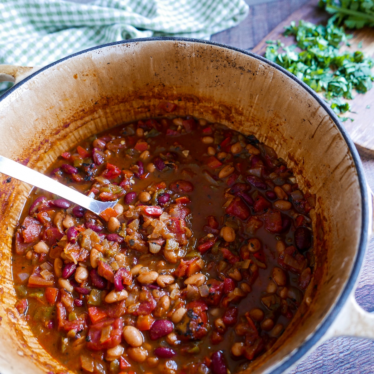 large pot of vegetarian chili with ladle and chopped cilantro in background.