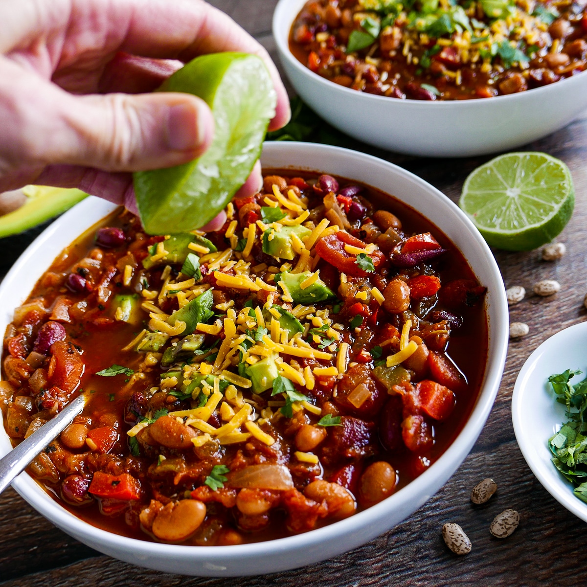 white hand squirting lime over bowl of chili with another bowl in background.