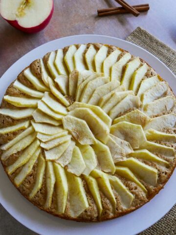 dutch apple cake on a white platter with apple halves in background