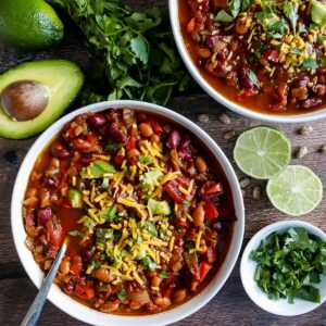 two bowls of vegetarian chili with cilantro lime and avocado scattered on table