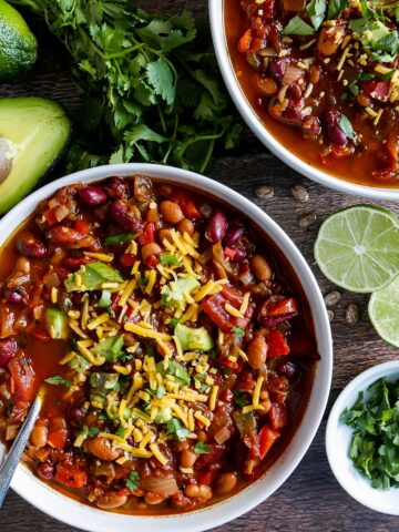 two bowls of vegetarian chili with cilantro lime and avocado scattered on table