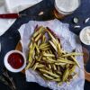 roasted japanese sweet potato fries on a cuttingn board with ketchup and glass of beer in background