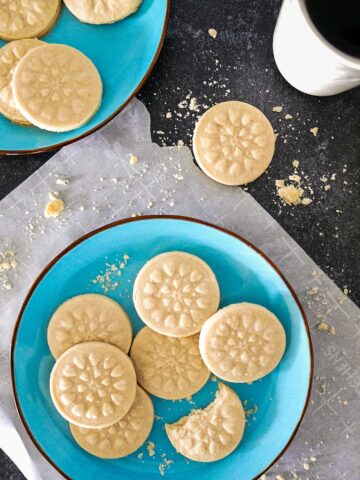 cardamom shortbread cookies arranged on two blue plates with cup of coffee in background