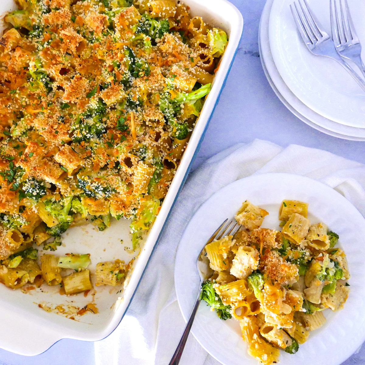broccoli-pasta-bake-in-pan.jpg broccoli pasta bake on a white plate and in a baking dish with two forks and white napkin