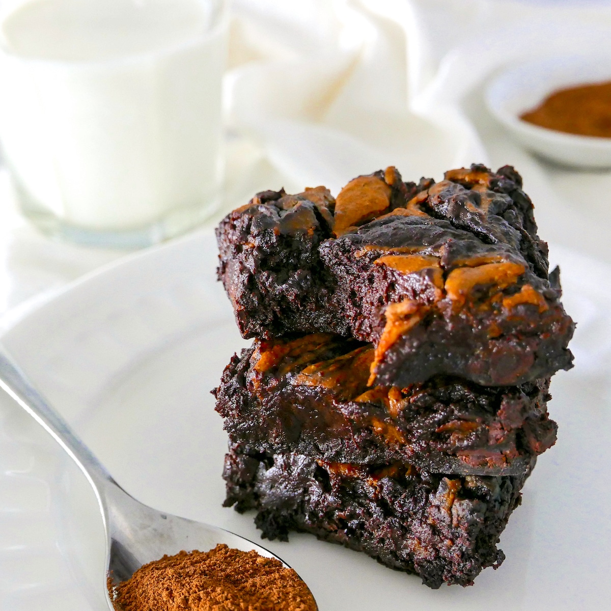 vegan-pumpkin-brownies.jpg vegan pumpkin brownies stacked on a white plate with a spoon of cinnamon.