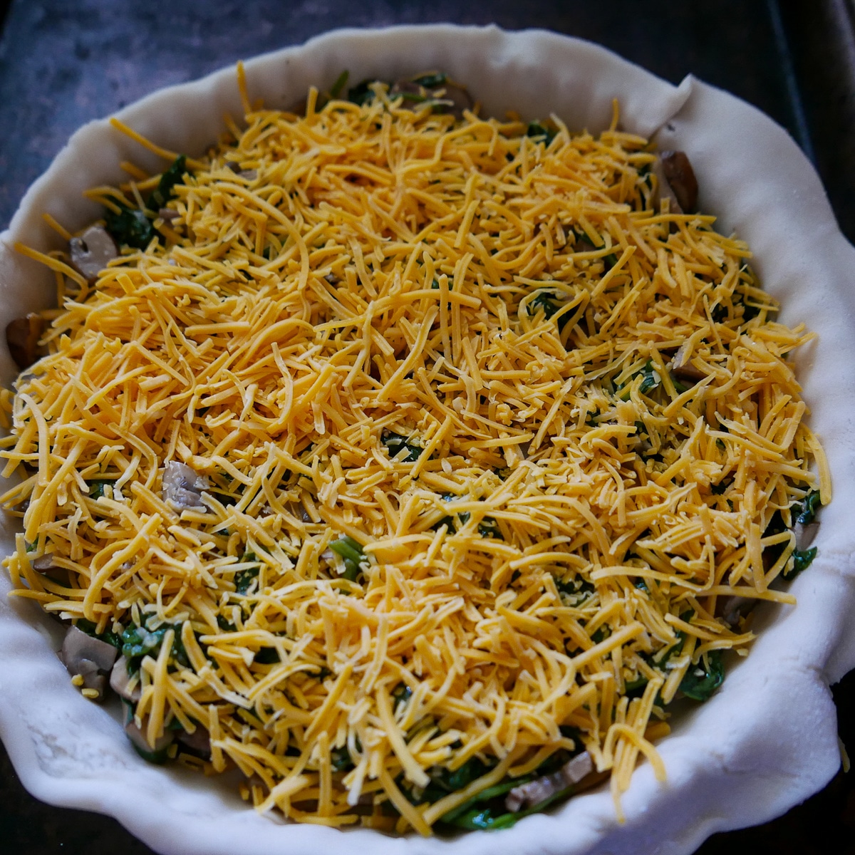 cheddar cheese on top of spinach and mushrooms in a tart pan.