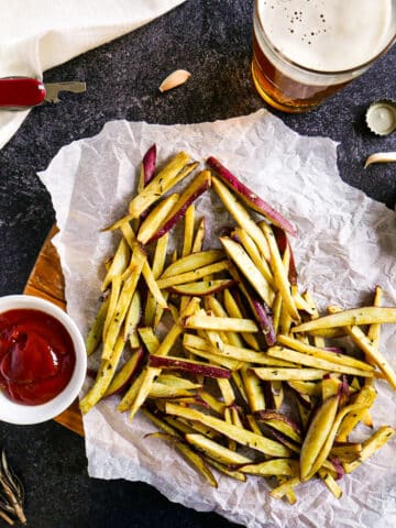 Roasted japanese sweet potato fries on a wooden cutting board with beer and condiments.