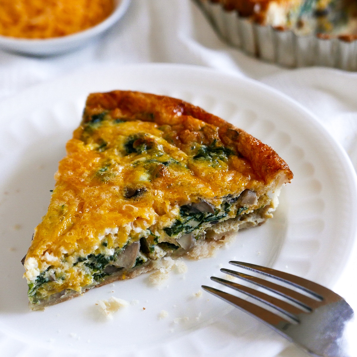 piece of spinach and mushroom quiche on a white plate with fork.