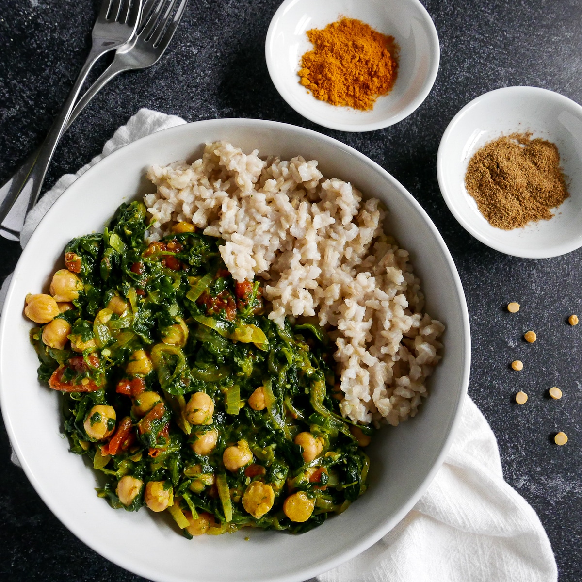 white bowl with spinach chickpea curry and brown rice resting on a white napkin.