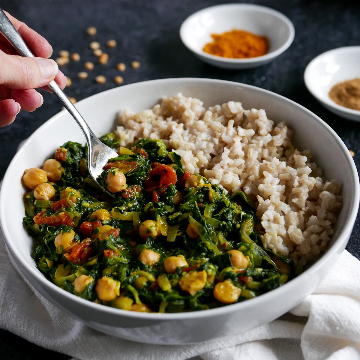 Fork digging into bowl of vegan chickpea curry with brown rice.