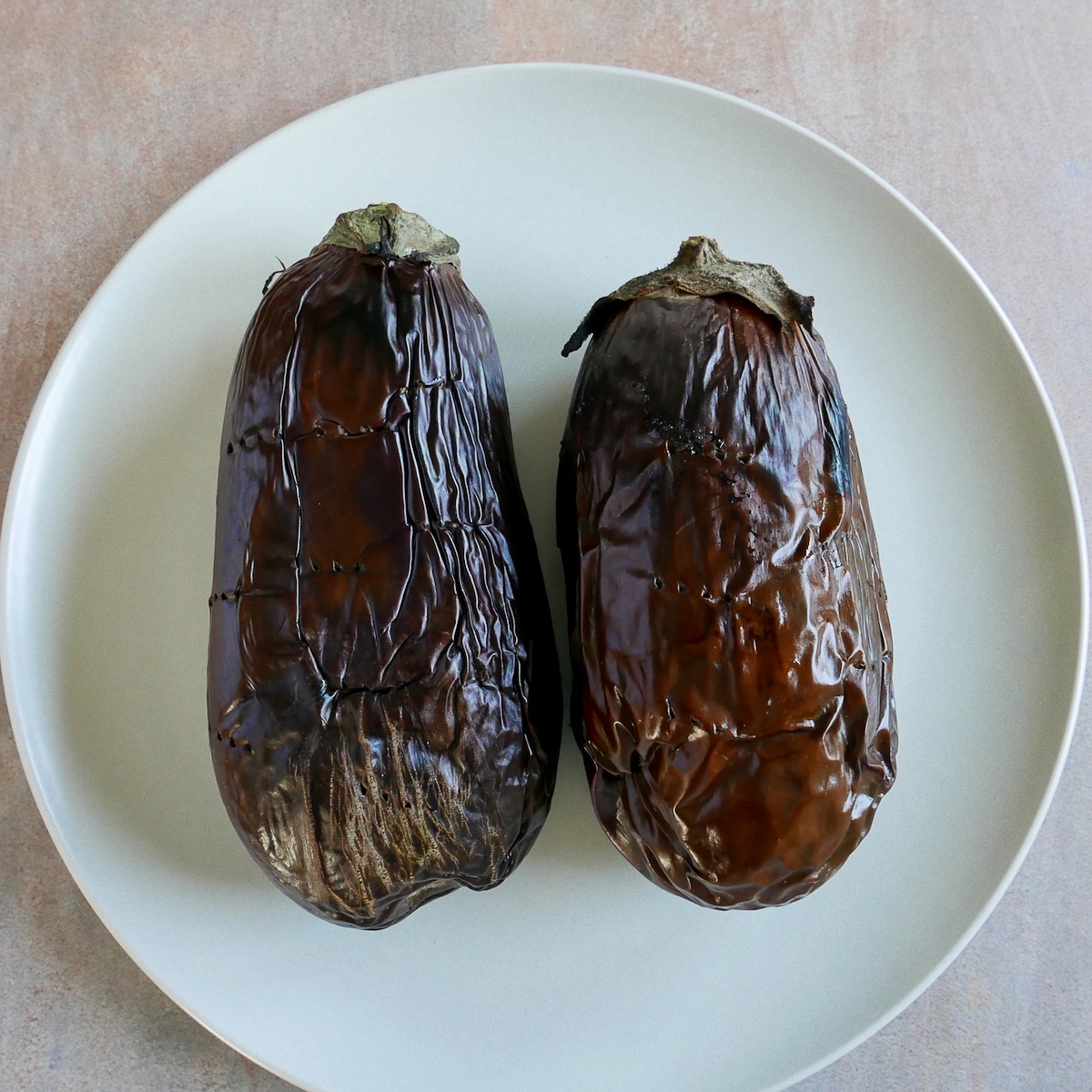 two roasted eggplants on a white platter.