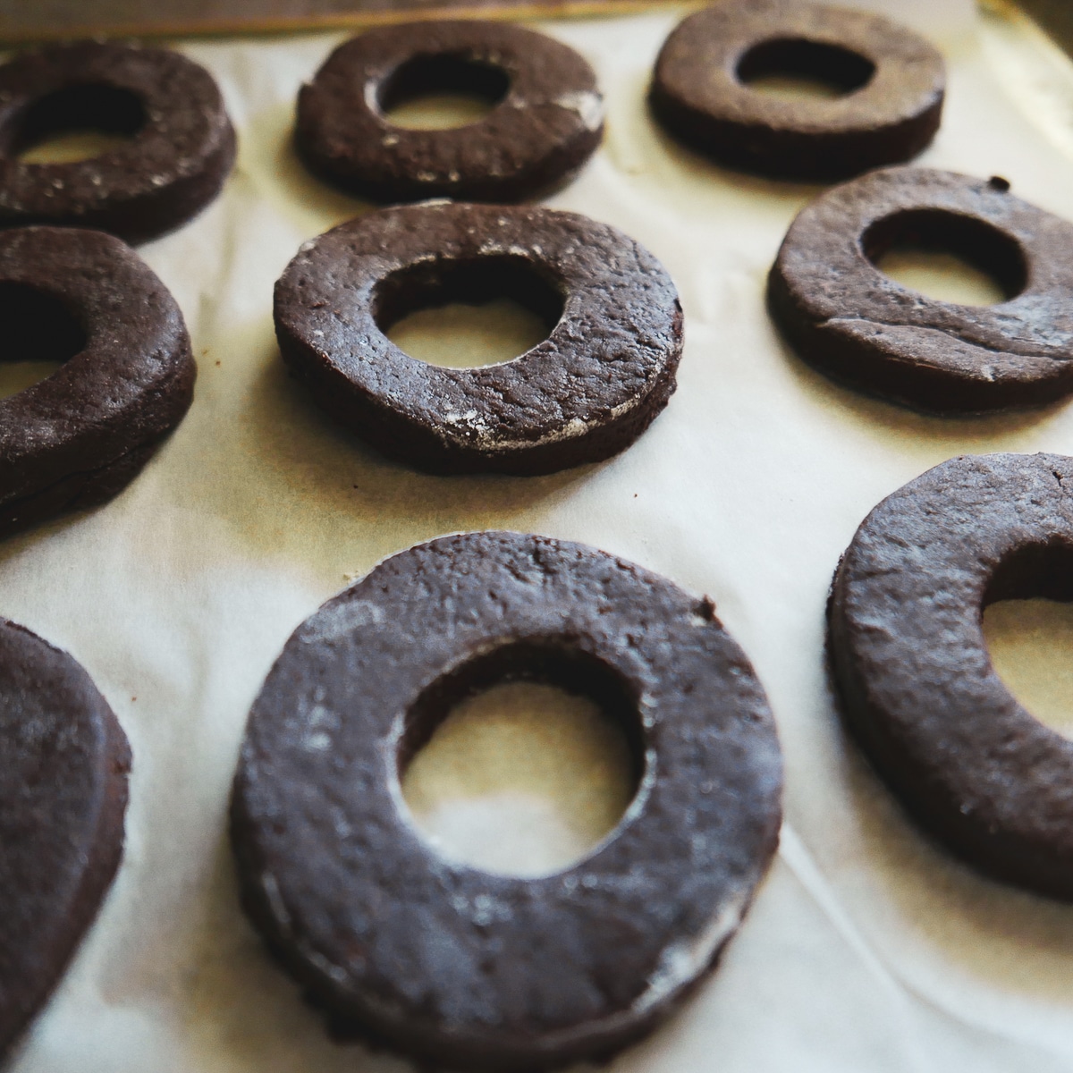 chocolate old fashioned donuts cut out and resting on baking sheet.