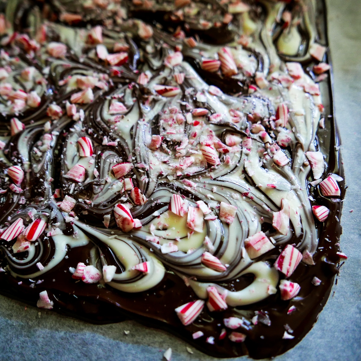 Crushed candy canes sprinkled onto melted chocolate on a baking sheet.