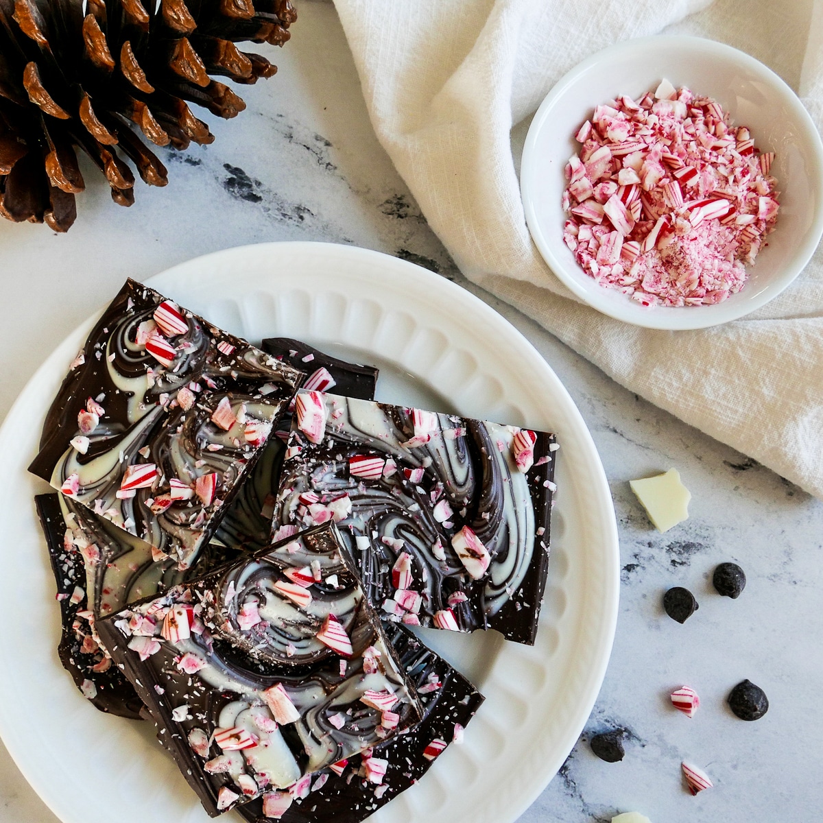 Peppermint bark on a white plate with cup of crushed peppermint.