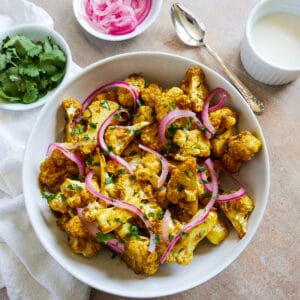 Bowl of tandoori cauliflower with cup of yourt sauce in the background.