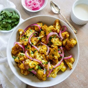 Bowl of tandoori cauliflower with cup of yourt sauce in the background.