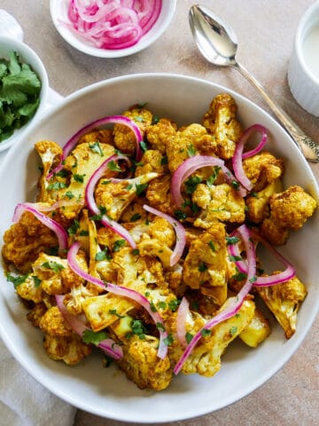 Bowl of tandoori cauliflower with cup of yourt sauce in the background.