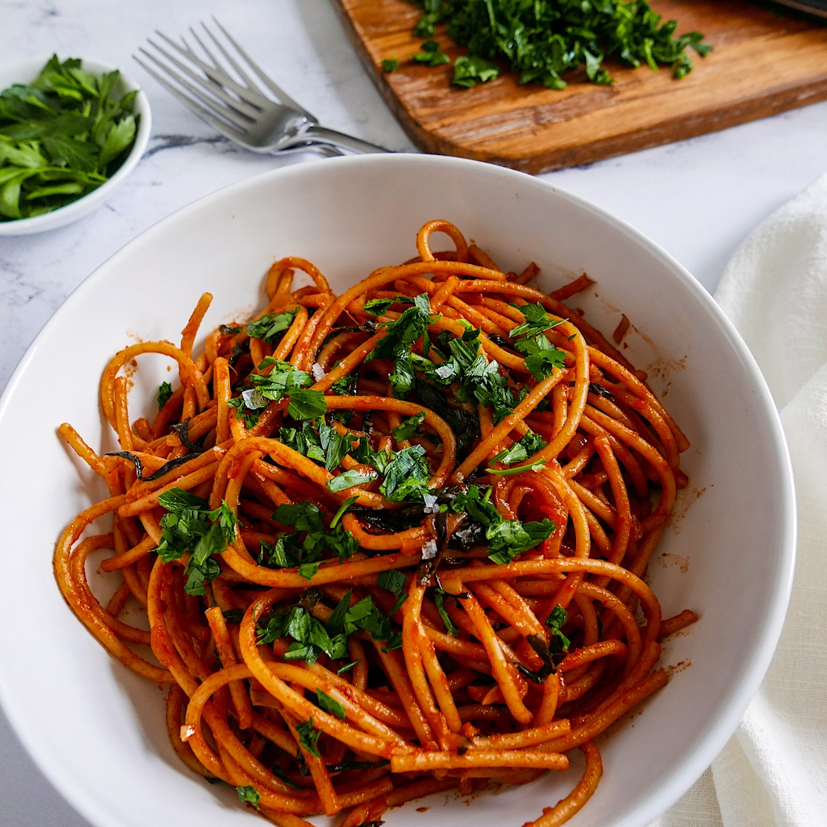 caramelized shallot pasta with greens in a white bowl with forks and parsley in background.