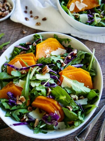 roasted squash salad in a white bowl with two forks on a table.