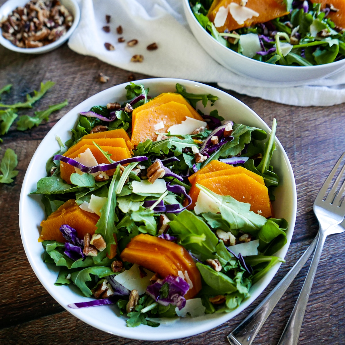 roasted squash salad in a bowl with two forks on table and salad in background.