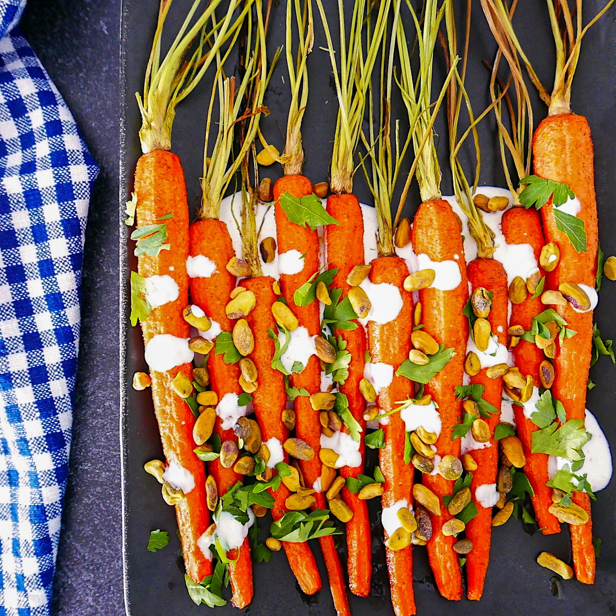 cumin roasted carrots with yogurt sauce on a platter with gingham napkin next to it.