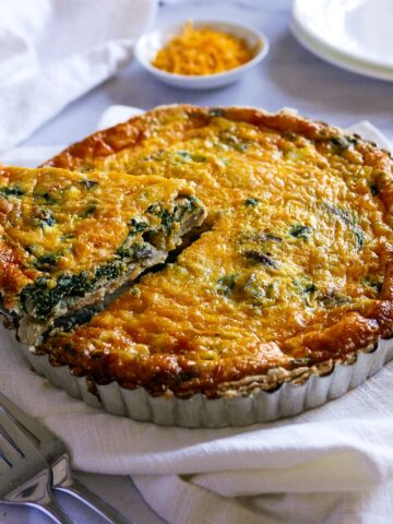 cheesy spinach and mushroom quiche in a tart pan with one piece being lifted out