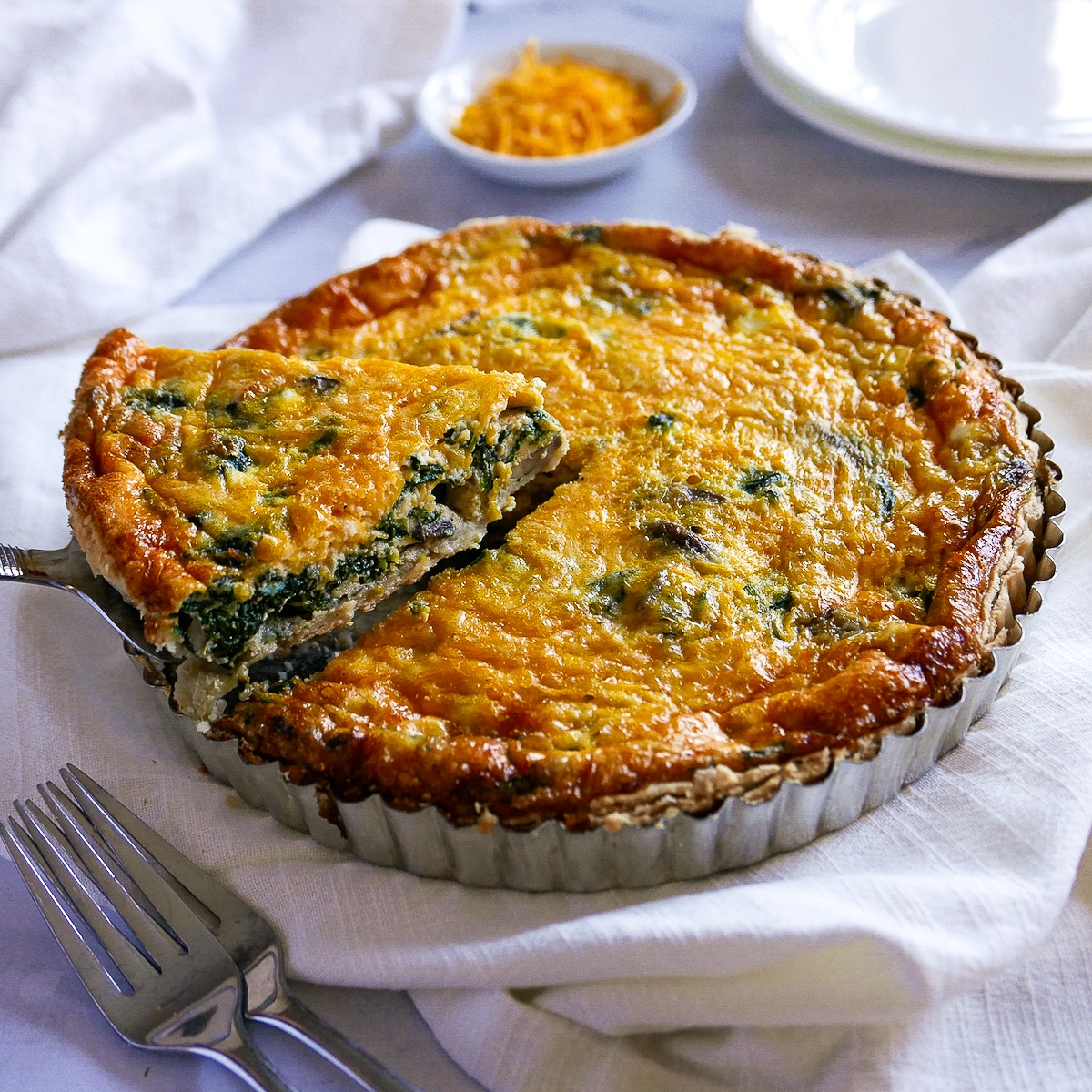 Spinach and mushroom quiche with a pie server lifting out one piece from pie pan.