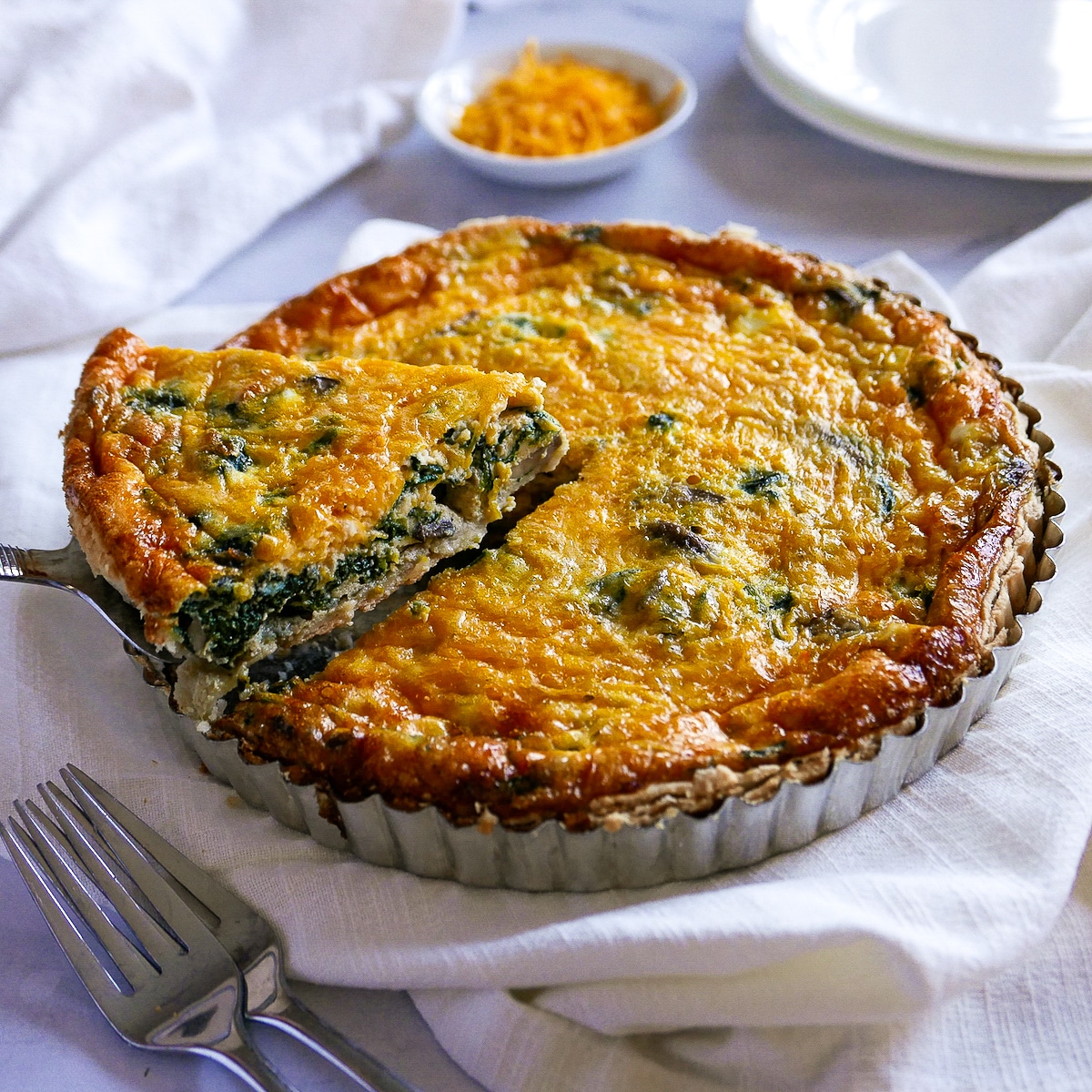 cheesy-spinach-and-mushroom-quiche.jpg Spinach and mushroom quiche with a pie server lifting out one piece from pie pan.