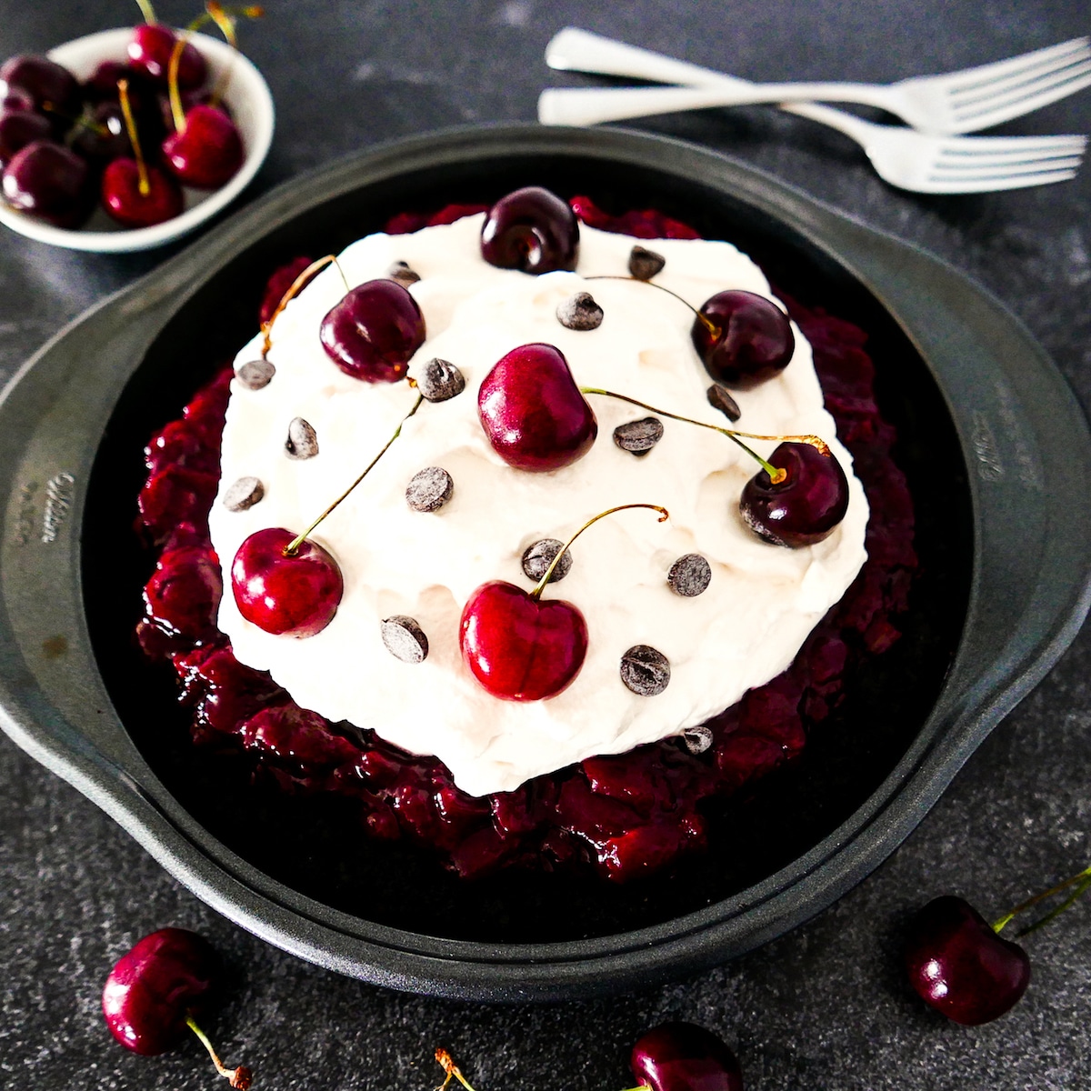 black forest pie in pie pan with cup of cherries and forks in the background.